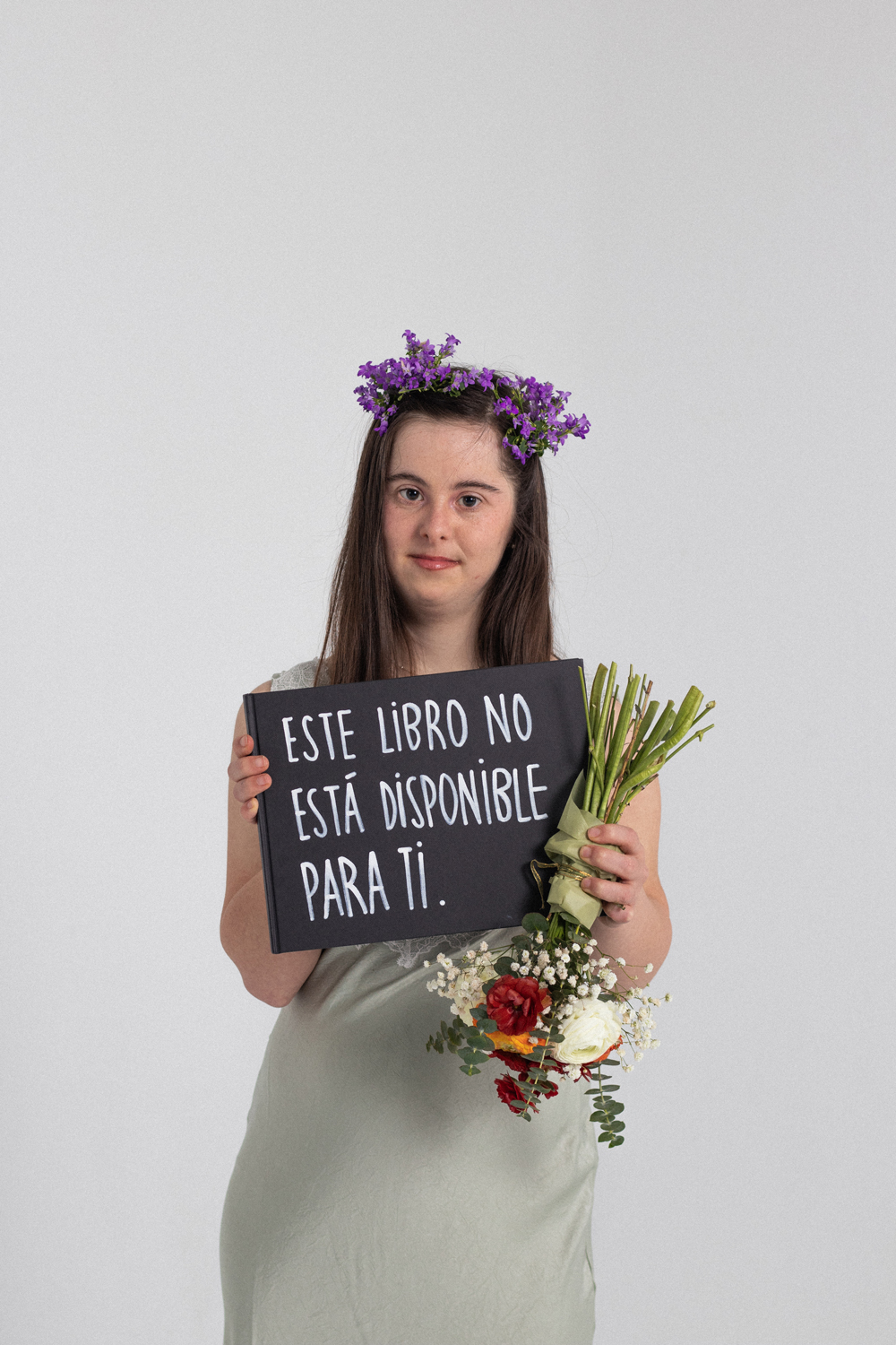 Arianna-Teatre Sense Límits-EÒLIA CSAD Una dona amb una corona de flors morades i un ram de flors de colors mira cap a l'esquerra sobre un fons blanc.