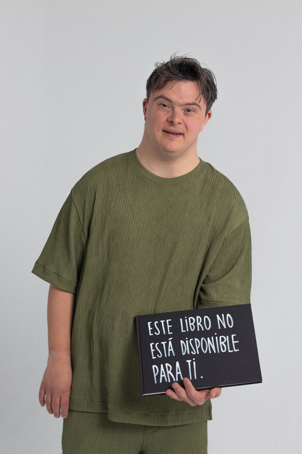 Bernat-Teatre Sense Límits-EÒLIA CSAD Un home amb una samarreta verda sosté un cartell que diu "Aquest llibre no està disponible per a tu" sobre un fons blanc.