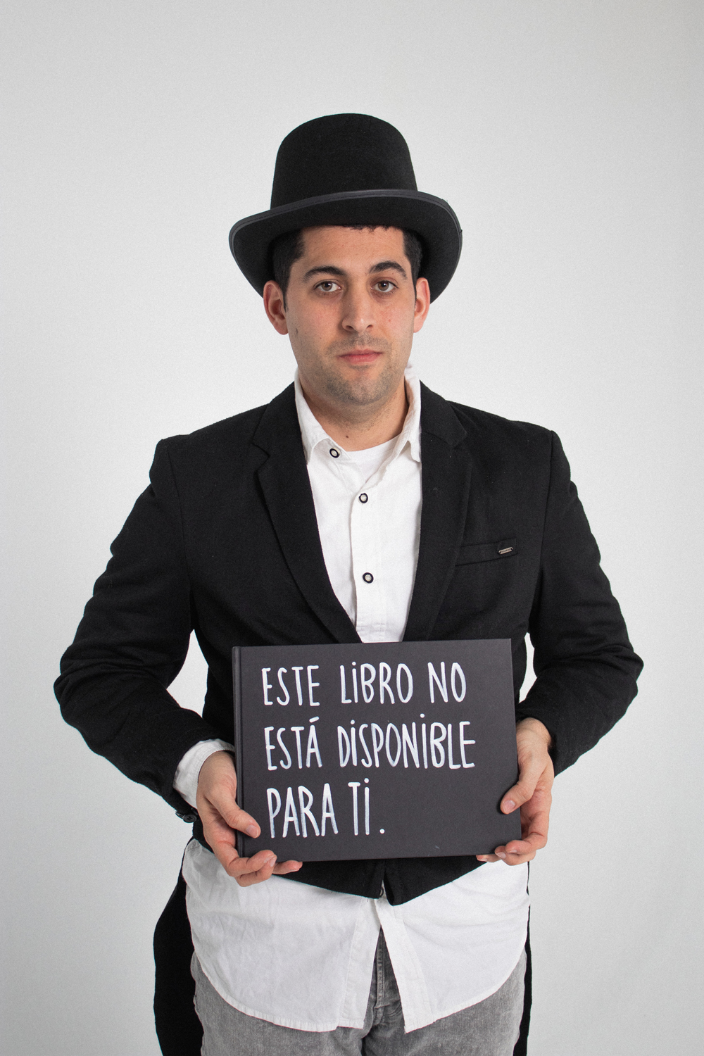 Jaume-Teatre Sense Límits-EÒLIA CSAD Un home amb barret negre i americana sosté un cartell que diu "Aquest llibre no està disponible per a tu" sobre un fons blanc.