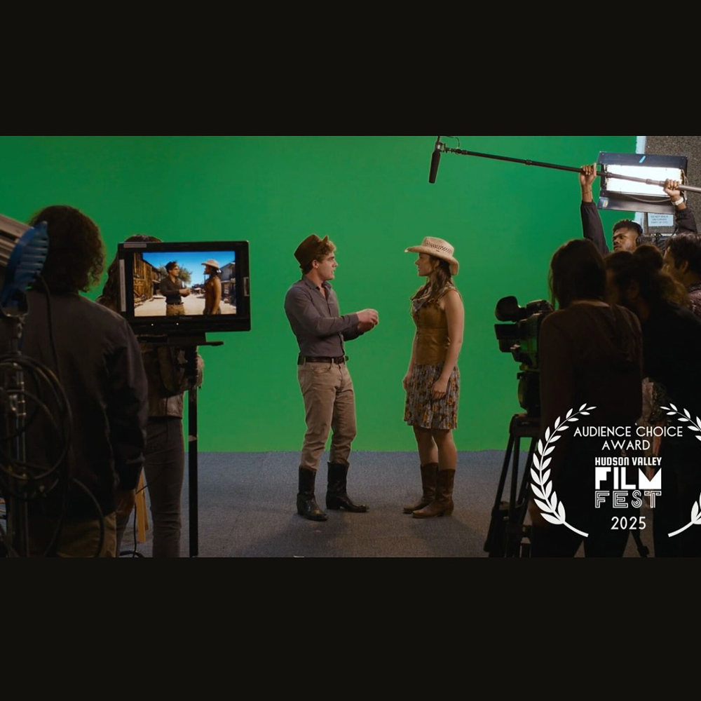 Imatge d'un rodatge cinematogràfic amb dos actors vestits d'estil western, davant d'una pantalla verda (croma) en un estudi. L'equip tècnic, incloent càmeres, monitors i personal de so i il·luminació, és visible al voltant de l'escena. Es promociona l'Audience Choice Award del Hudson Valley Film Festival 2025.