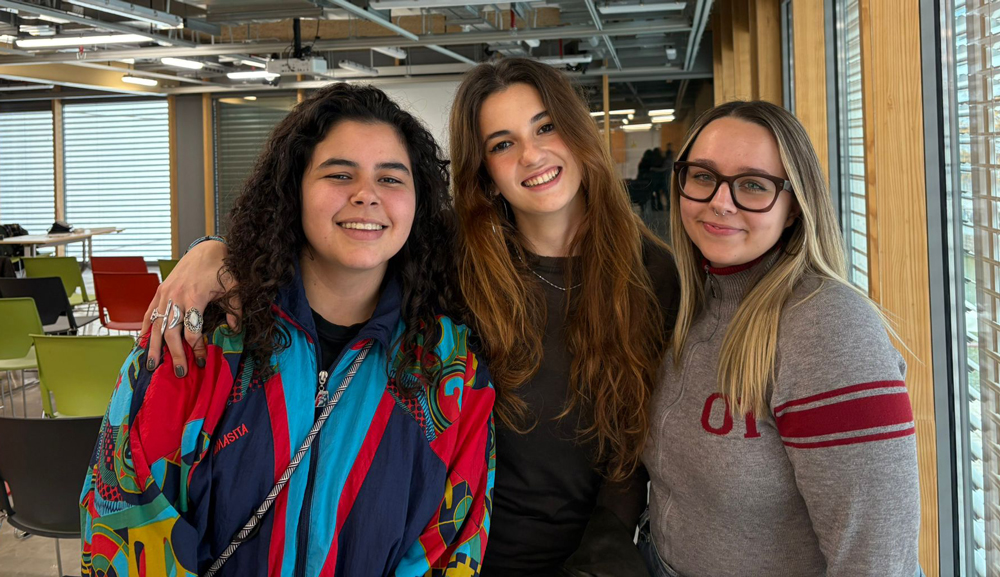 L’alumnat-de-Direcció-escènica-i-dramatúrgia-del-Grau-col·labora-a-la-nova-edició-Òh!pera Tres estudiants de Direcció escènica i dramatúrgia somriuen davant de la càmera, la noia de l'esquerra porta una jaqueta esportiva de colors vius, la del centre té el cabell llarg i castany, i la de la dreta porta ulleres i un jersei gris.