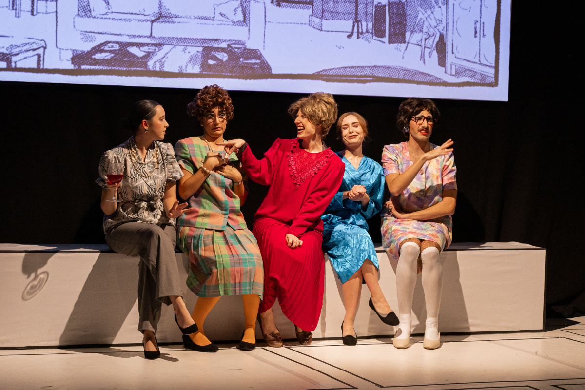 Cinc actors i actrius de l'obra "No es pot saber" asseguts a l'escenari del Teatre Eòlia, vestits amb roba i estètica d'època, interactuant durant una escena davant d'una pantalla amb projeccions.